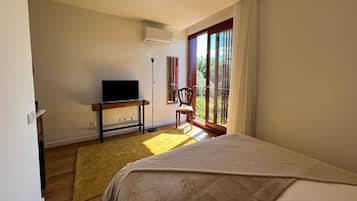 Un dormitorio con cama, televisor sobre un mueble de madera, una silla junto a la ventana y un balcón con vistas.