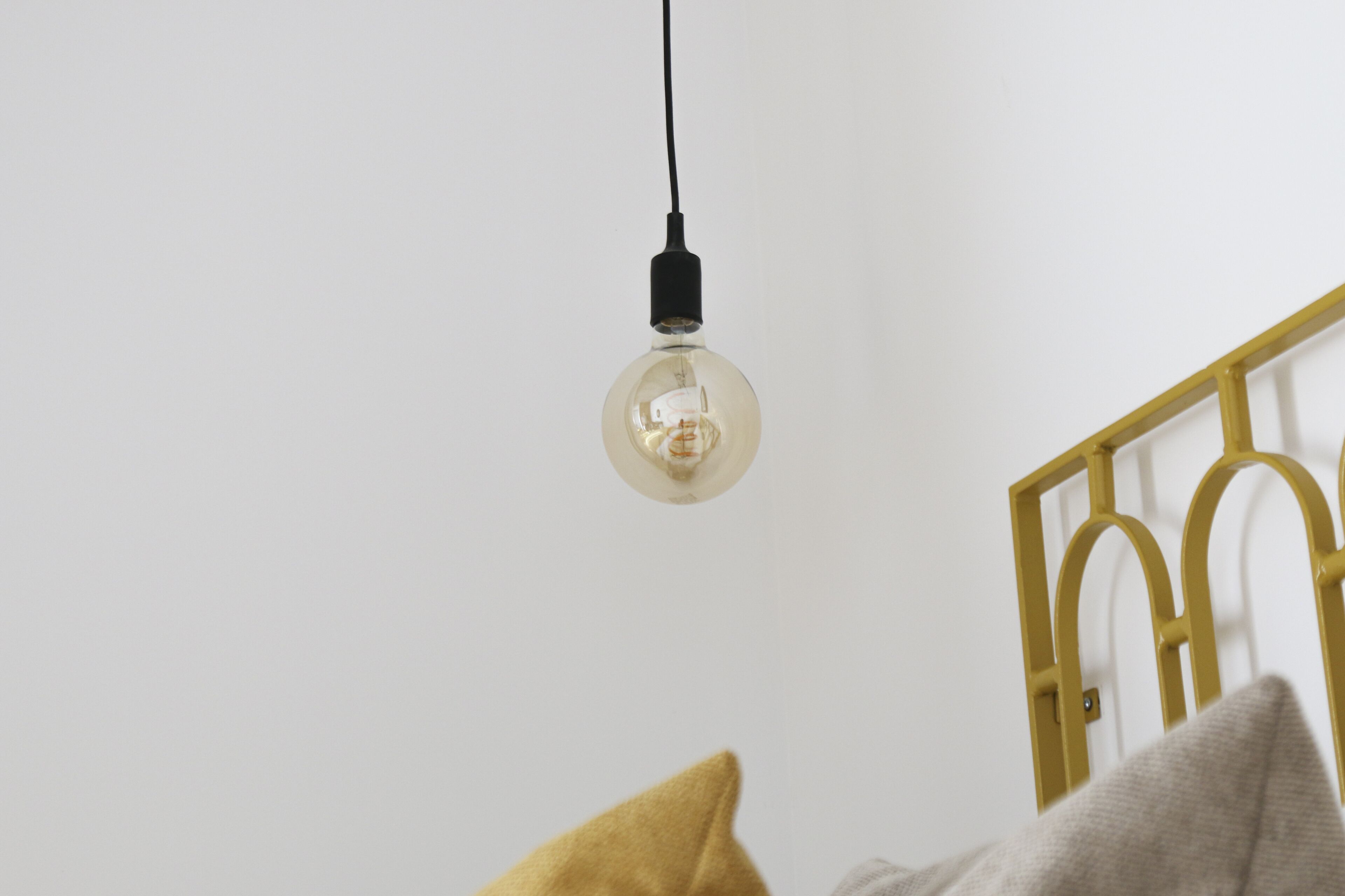 A room with a hanging light bulb, a yellow pillow, and a white wall.