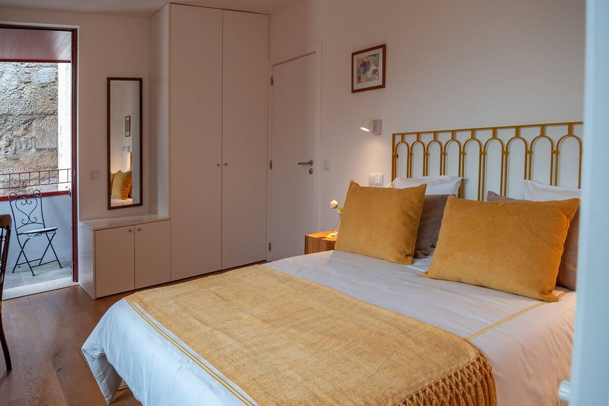 Een slaapkamer met een bed, nachtkastje, spiegel, kledingkast en raam met uitzicht.