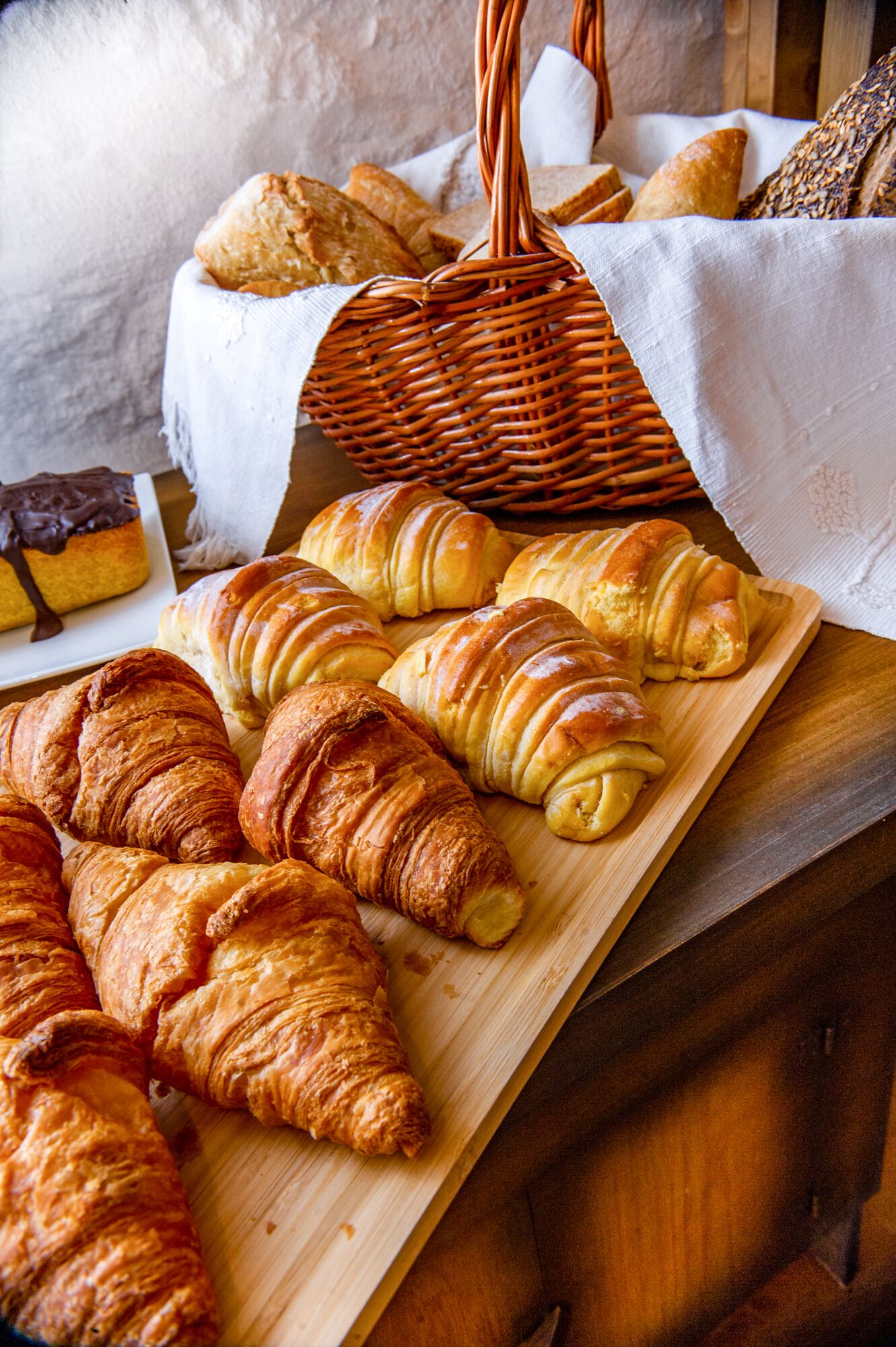 A wooden table with various baked goods, including croissants and bread, displayed on a white cloth.