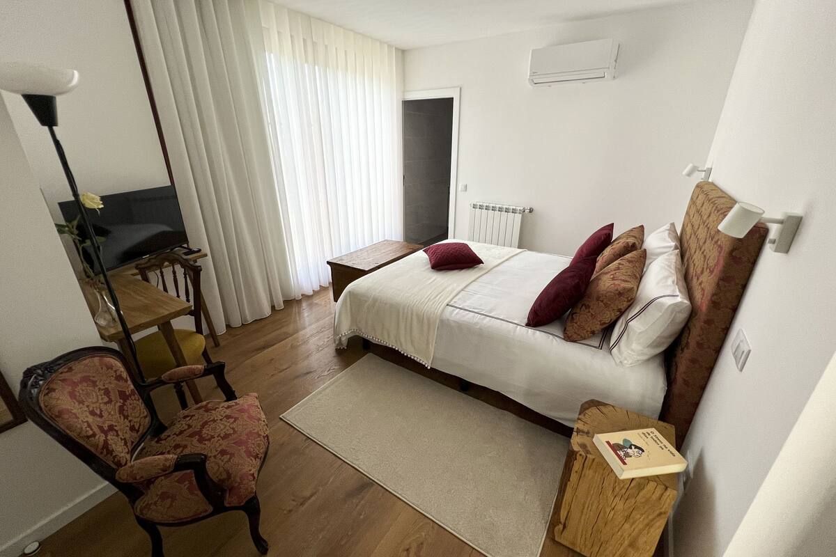Een slaapkamer met een bed, een stoel, een nachtkastje, een radiator en een televisie.