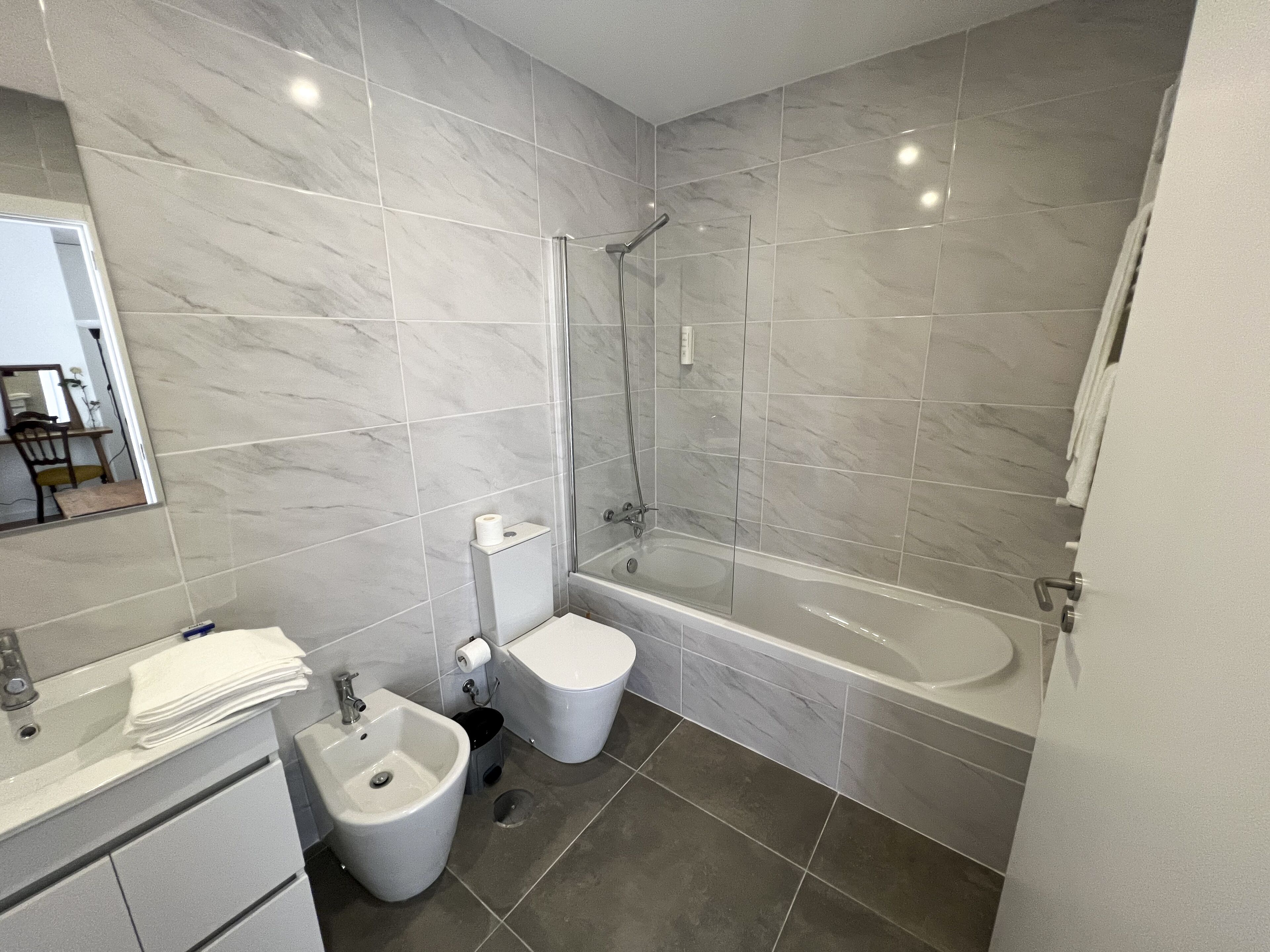 Een moderne badkamer met een bad, toilet, hygiëneschuimer en wastafel.