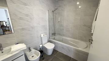 Een moderne badkamer met een bad, toilet, hygiëneschuimer en wastafel.