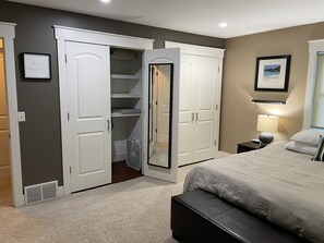 Un dormitorio con cama, mesita de noche con lámpara, tocador y un amplio vestidor con puertas abiertas.