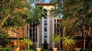Un hotel de varios pisos con un patio central, rodeado de abundante vegetación y palmeras.