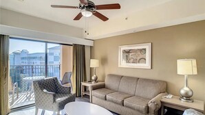 Una habitación de hotel con balcón, ventilador de techo, sofá, mesa de centro y dos lámparas.