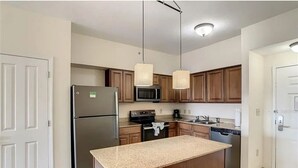 Una cocina con armarios de madera, un refrigerador de acero inoxidable, un microondas y un lavamanos.