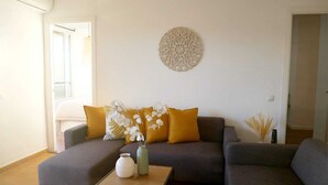 Ein Wohnzimmer mit grauem Sofa, zwei gelben Kissen, einer weißen Vase und einer Wanddekoration.