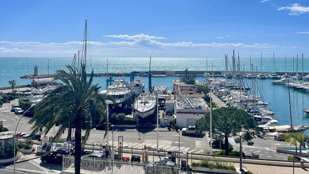 Un puerto deportivo con barcos amarrados, un faro y un cielo azul despejado.