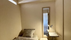 Un dormitorio pequeño y moderno con una cama individual, una mesita de noche, un espejo y un escritorio con lámpara.