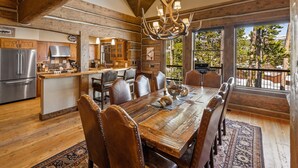 A rustic kitchen with wooden beams, a large dining table, and a chandelier. - Luxury Powder Ridge Cabin - Ski-In/Ski-Out Access (Big Sky)