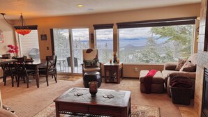 Una sala de estar acogedora con chimenea, comedor y ventanas amplias que ofrecen vistas a montañas nevadas.