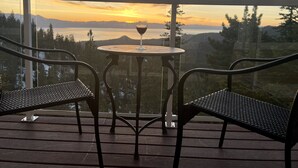 Un balcón con dos sillas y una mesa, con vistas panorámicas a montañas y un lago al atardecer.
