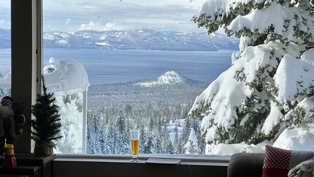Habitación con vista a un paisaje nevado, un árbol de Navidad y una cerveza en el alféizar de una ventana.