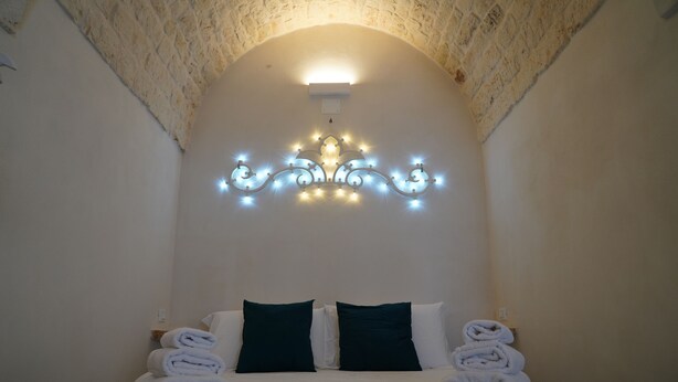 A hotel room with a bed, two pillows, a wall-mounted light fixture, and a textured ceiling.