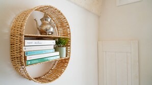 A woven shelf with books and a small plant, mounted on a wall next to a white door.