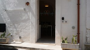A doorway leading into a room with a table and chairs, a white wall with a textured surface, and two potted cacti on the ground.