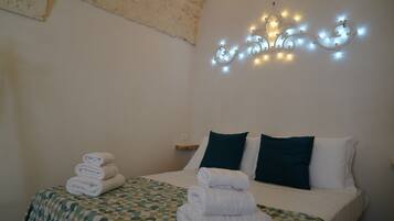 Un letto rifatto con cura, con una coperta a motivi decorativi, una pila di asciugamani piegati e un elegante applique.
