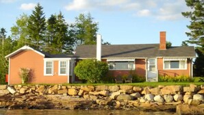 A two-story house with a stone retaining wall in front. - Cozy Waterfront Cottage, Henry Cove. Winter Harbor (Winter Harbor)