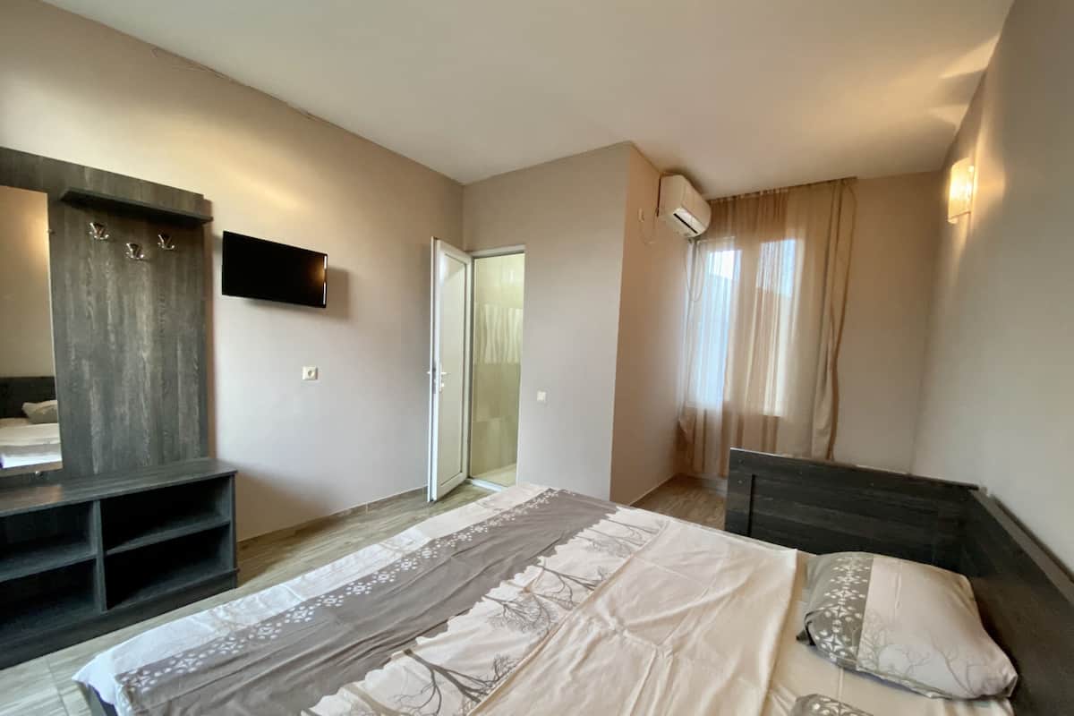 A bedroom with a bed, a wardrobe, a television, and an air conditioning unit.