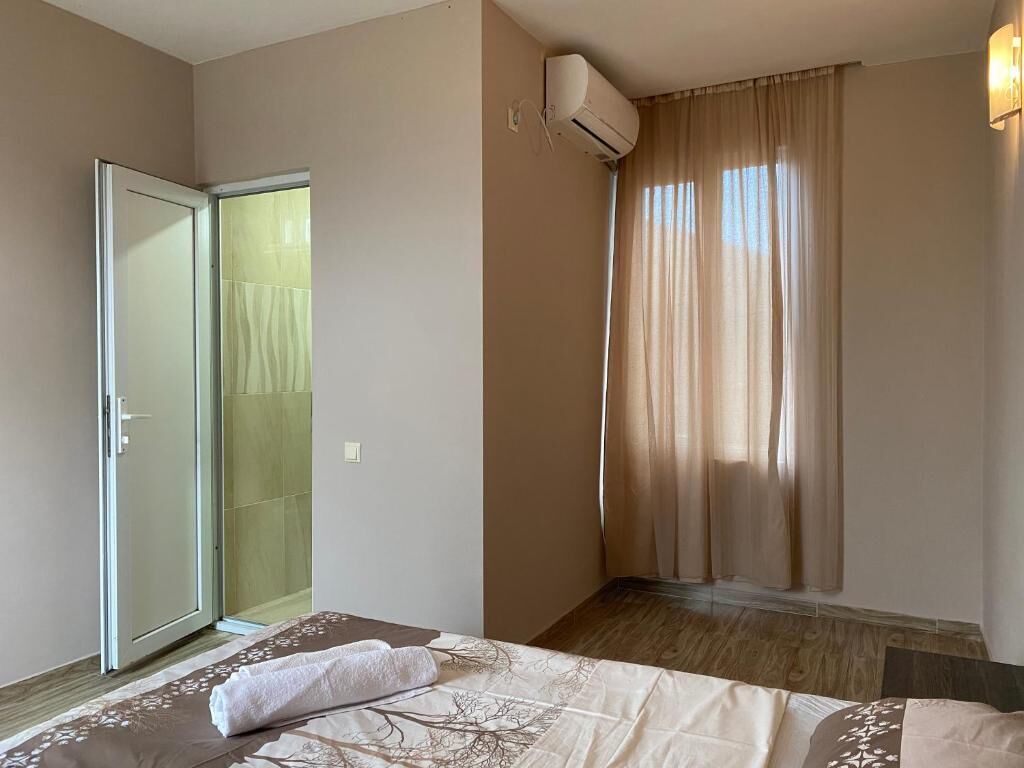 A hotel room with a bed, a sliding glass door leading to a shower, and an air conditioning unit.