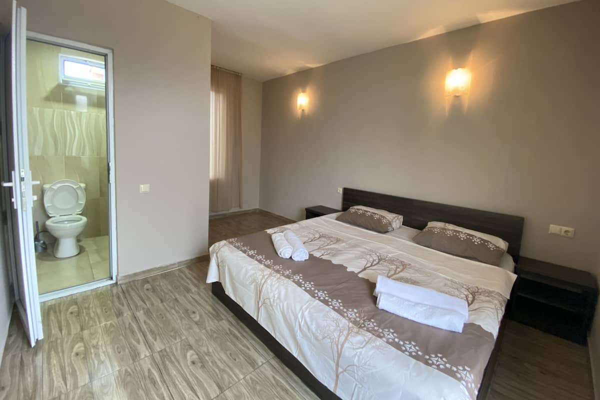A bedroom with a bed, a nightstand, a wall-mounted light, and a bathroom with a toilet and shower.