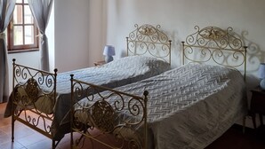 A room with two beds, a window with curtains, a lamp, and a wall-mounted light fixture. - Family apartment near the medieval castle (Bracciano)