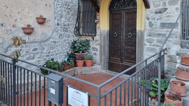 A stone building with a yellow archway and a wooden door, potted plants, and a sign indicating a tourist accommodation. - Family apartment near the medieval castle (Bracciano)