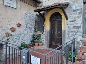 Un bâtiment en pierre avec une arche jaune et une porte en bois, des plantes en pot et une enseigne indiquant qu’il s’agit d’un hébergement touristique.