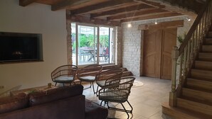 Een woonkamer met een bruine leren bank, rieten stoelen, een flatscreentelevisie en een stenen muur.