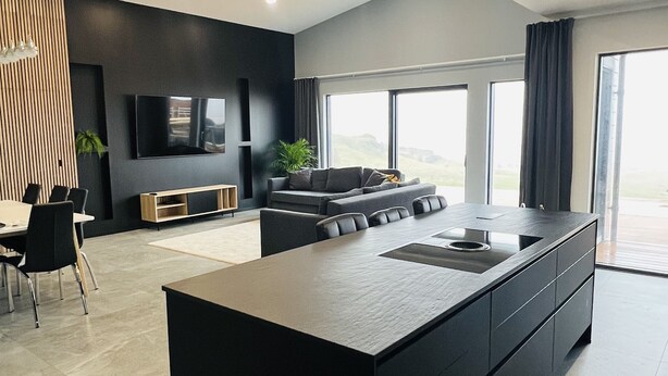 A modern kitchen with a large island, dark cabinetry, and a flat-screen TV mounted on the wall. - Spacious villa in Golden Circle with amazing view & hot tub! (Reykholt)