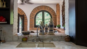 Una cocina con encimera de mármol, un fregadero y una ventana con vista a un muro de ladrillo y vegetación.