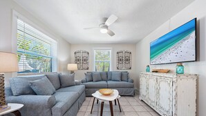 A living room with two grey sofas, a white coffee table, a white cabinet with decorative items, and a large TV on the wall. - Stunning Pool-side 2 bed/2 Bath With A Quick Walk to Beach!! (Sarasota)