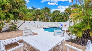 A poolside area with a white table and chairs, a pool, and palm trees. - Stunning Pool-side 2 bed/2 Bath With A Quick Walk to Beach!! (Sarasota)