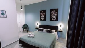 Un dormitorio moderno con una cama, dos mesitas de noche adosadas a la pared, una silla y una obra de arte.