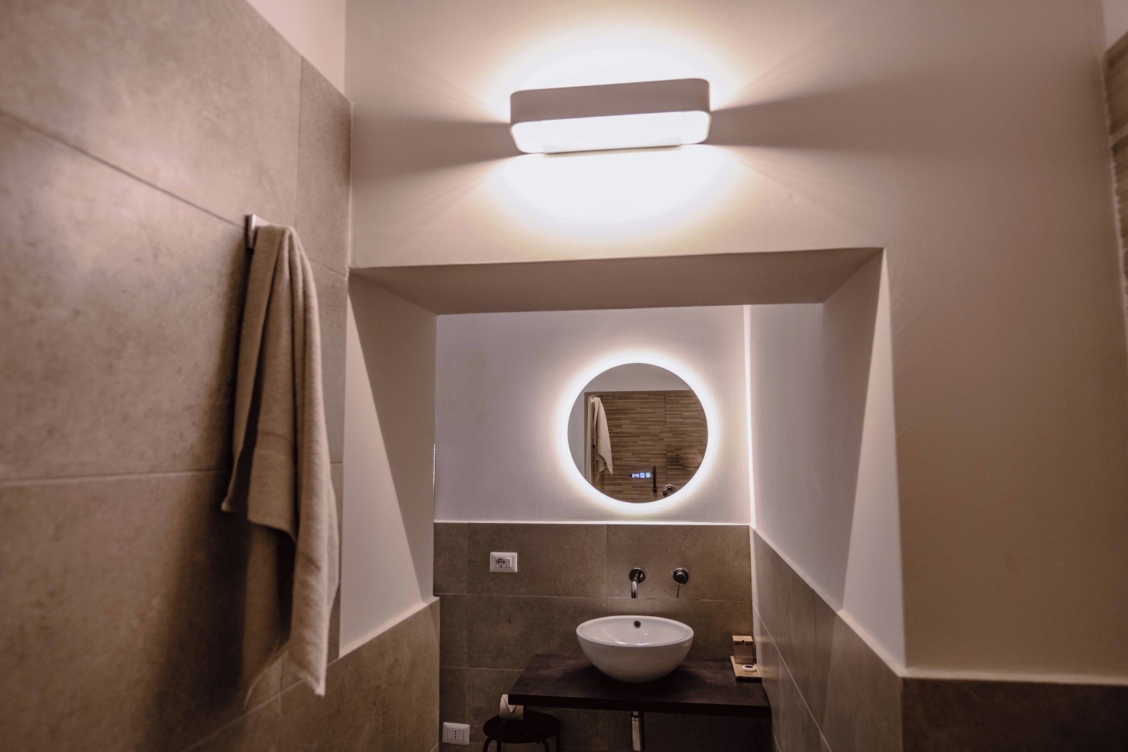Une salle de bain moderne avec un miroir rond, un lavabo sur colonne et une serviette accrochée au mur.