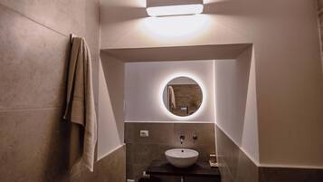 Une salle de bain moderne avec un miroir rond, un lavabo sur colonne et une serviette accrochée au mur.