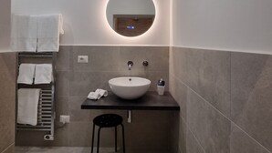 Un baño moderno con un espejo redondo, un lavamanos blanco y un perchero para toallas.