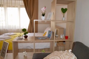 Ein kompaktes Hotelzimmer mit Stockbett, Schreibtisch mit Topfpflanze, kleinem Tisch und einer Couch.