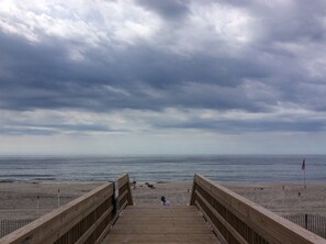 A wooden boardwalk leading to a beach with a cloudy sky.