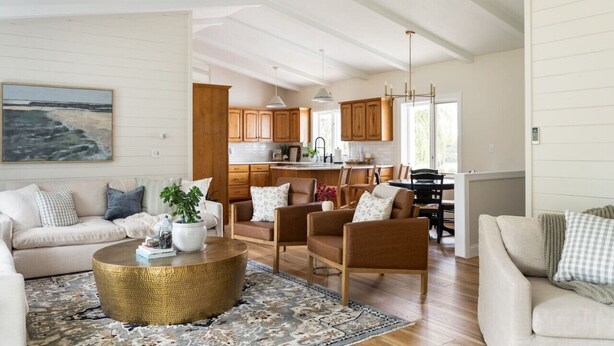 A spacious living room with a large round coffee table, a sofa, and a chair. There is a kitchen area with wooden cabinets and a dining table. - Sweet Shady Lane - Wine Country (Traverse City)