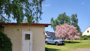 Pieni rakennus, jossa on punainen katto, valkoinen ovi ja pysäköity auto sen edessä.