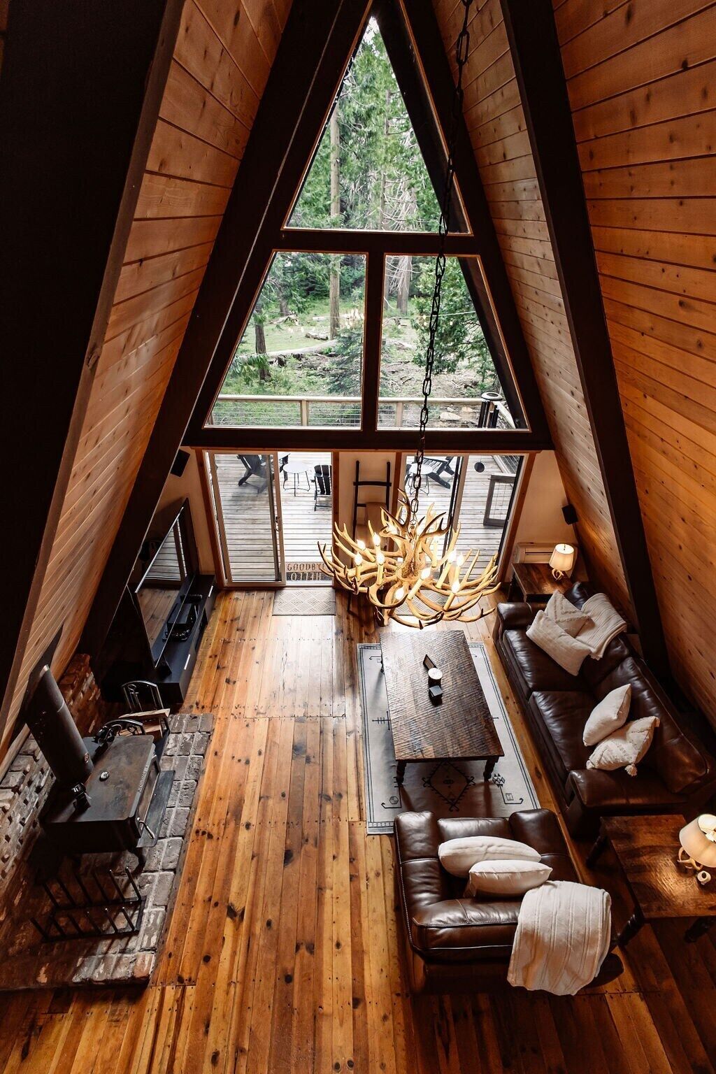 Une chambre à coucher confortable, aménagée en mezzanine, avec une grande fenêtre, un plancher en bois, un lustre, un canapé et une petite table.