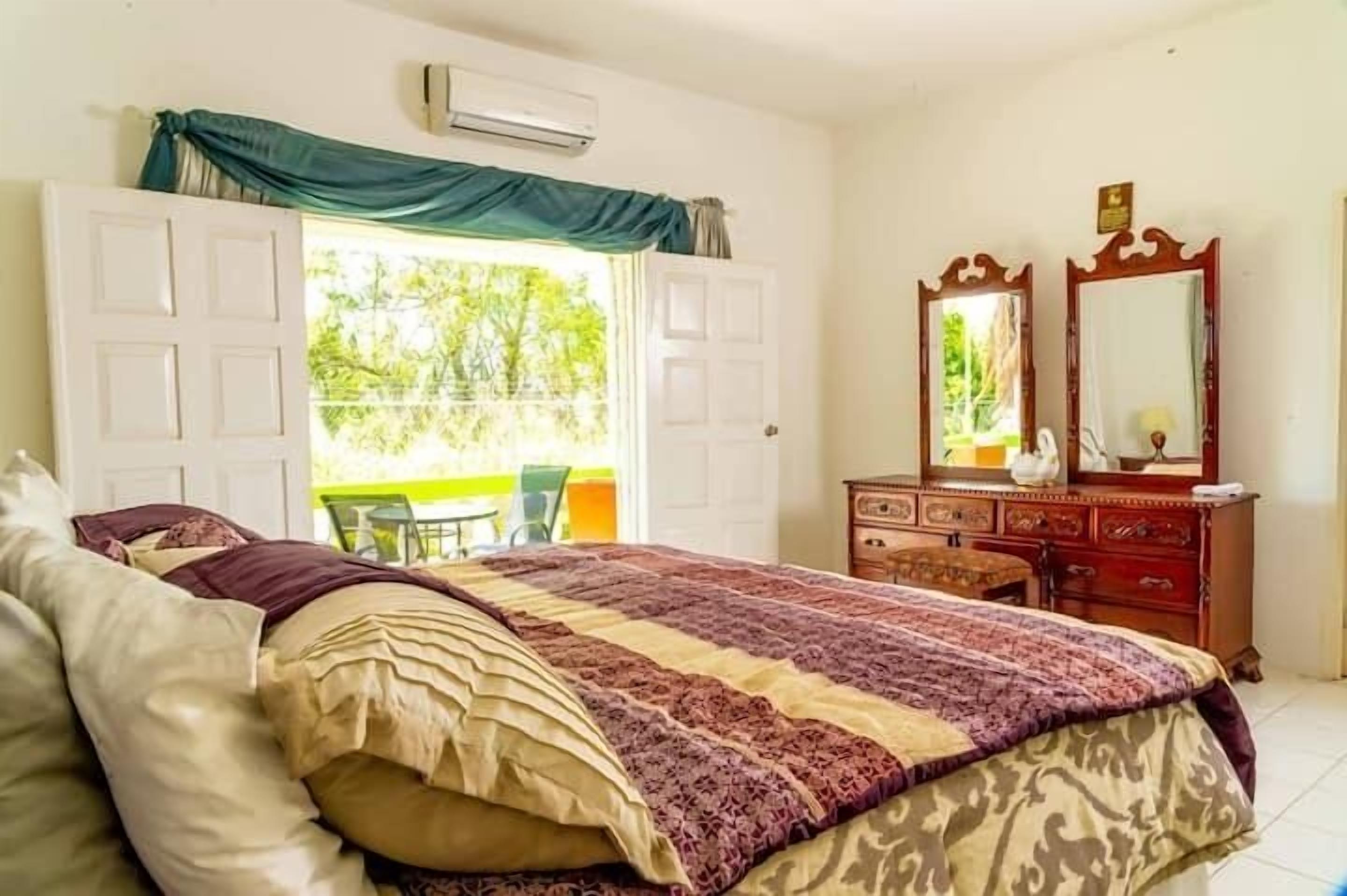 Un dormitorio con cama, cómoda, espejo y puerta abierta que da a un balcón.