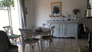 A dining area with a table and chairs, a cabinet with decorative items, and a window with curtains. - Maison Très Bien Située,dans Quartier Résidentiel.endroit Très Calme ,près Océan (Biscarrosse plage)