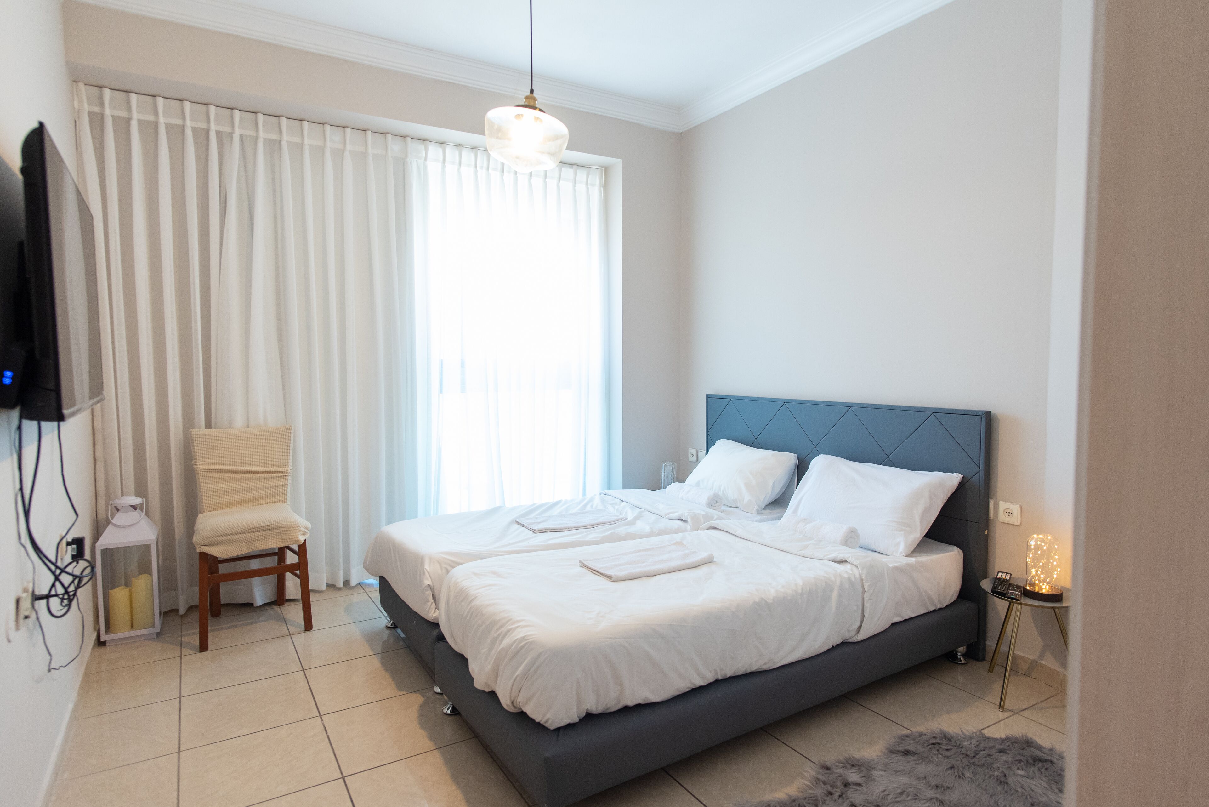 A bedroom with a large bed, a chair, a television, and a bedside table with a lamp.