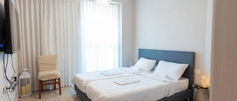 A bedroom with a large bed, a chair, a television, and a bedside table with a lamp.