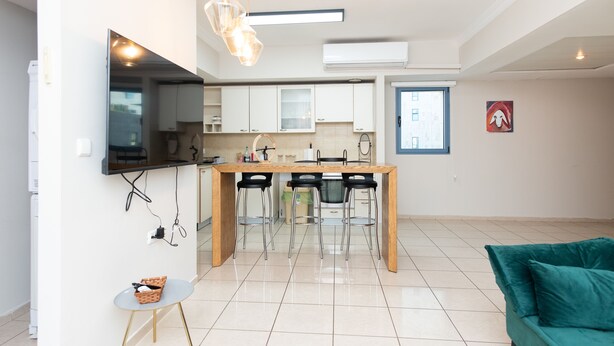A modern kitchen with a dining table, bar stools, and a TV mounted on the wall. - Mahane Yehuda Market Apartment Jerusalem (Jerusalem)
