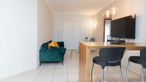 A modern kitchen with a wooden countertop, a black bar stool, and a green sofa with yellow cushions. - Mahane Yehuda Market Apartment Jerusalem (Jerusalem)