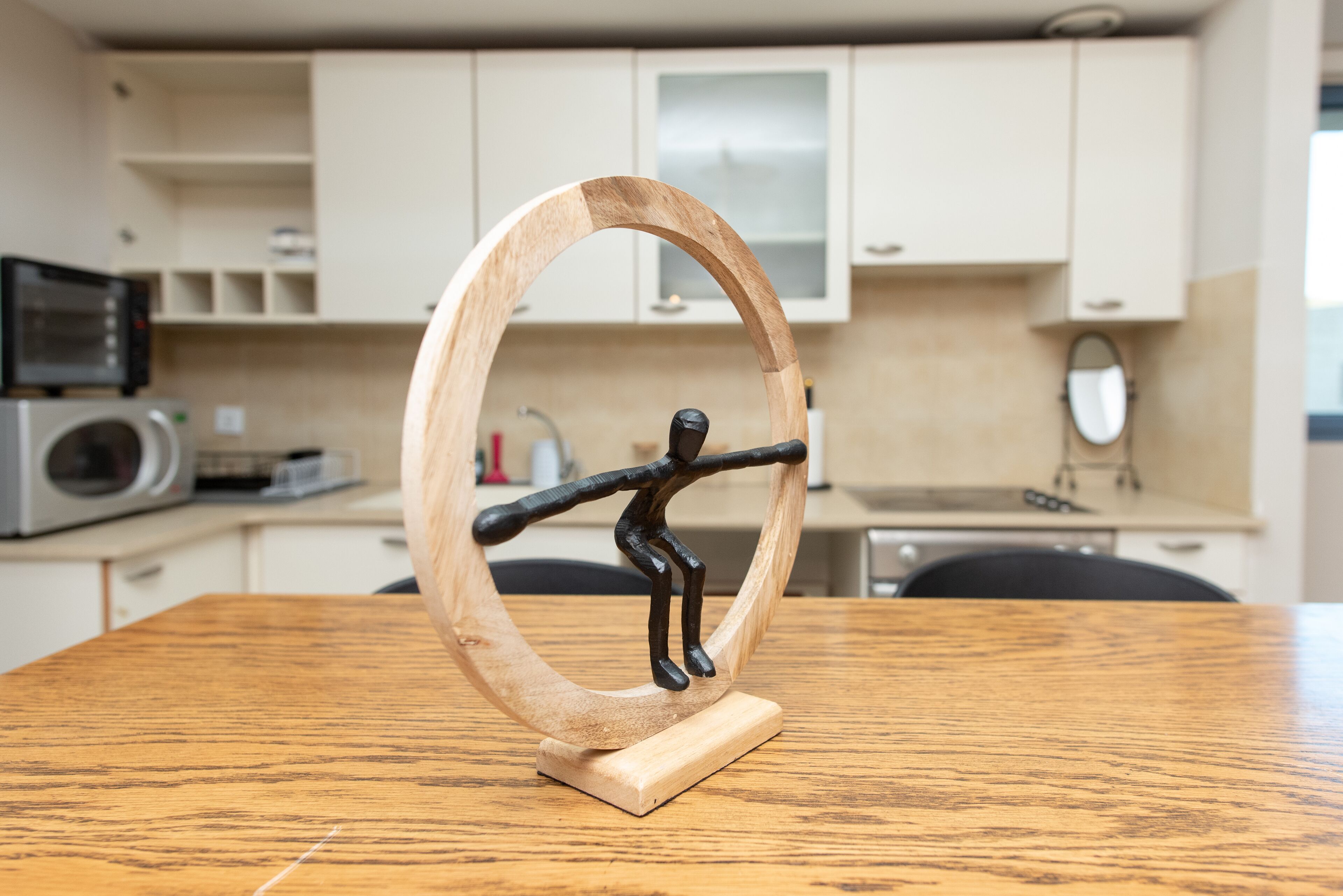 A wooden sculpture on a table in a modern kitchen with white cabinets and a microwave.